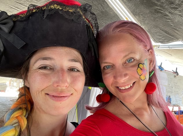 A self portrait of Amy Funk and her friend dressed in a fun hat and face paint smiling.